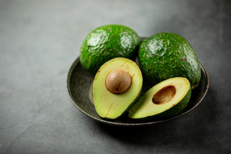 A perfectly ripe avocado half with its large pit, alongside sliced avocado pieces on a white plate.